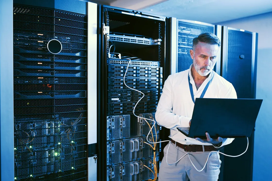 A technician using a laptop beside server equipment.
